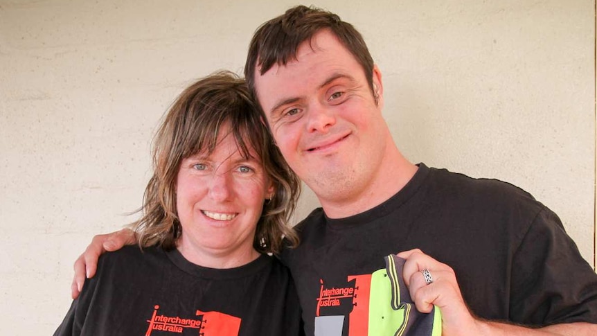 Woman and man grin at camera with heads leant together. Man has arm around woman, holding her close to him.