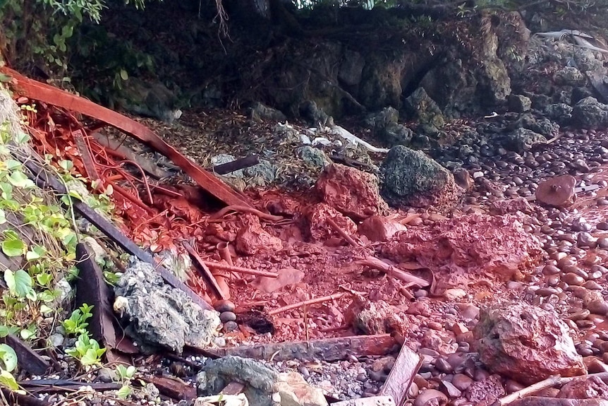 Red slurry from the mining spill turns part of the rocky shoreline at Basamuk Bay red.