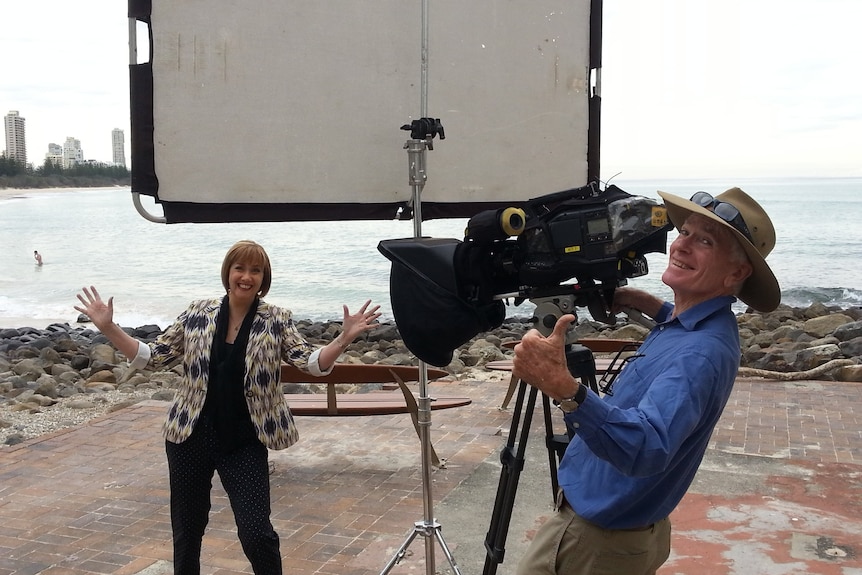 Woman with jazz hands standing in front of reflector board and camera as cameraman gives thumbs up.