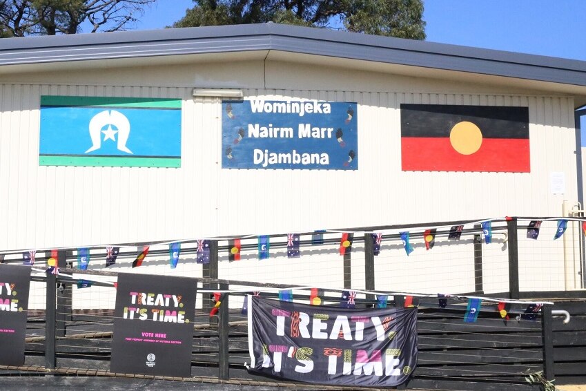 The Aboriginal and Torres Strait Islander flags are pinned to the outside of a shed beside a sign reading 'Wominjeka'.