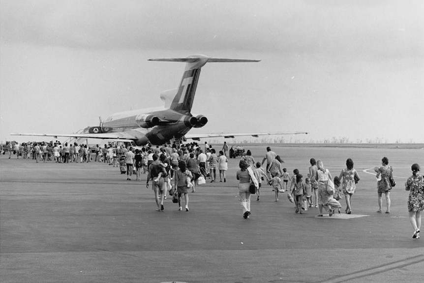 Black and white photo of evacuees walking across a tarmac to board a large airliner.