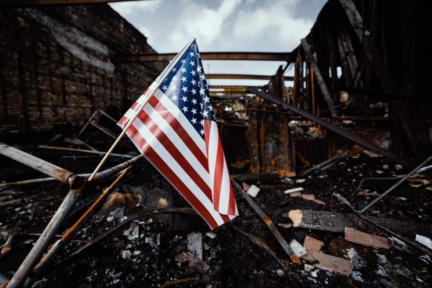 A United States flag hangs over a burnt down building.