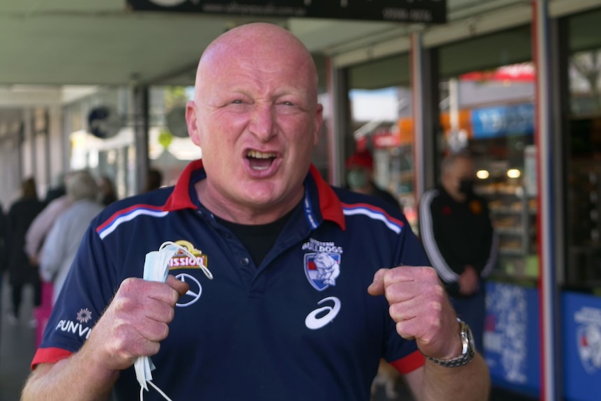 Chris Galea wears a Bulldogs top, he pumps his fists in front of a cafe painted in the club's colours