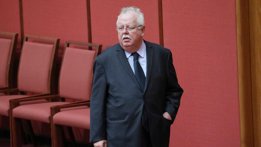 A full-length shot of Barry O'Sullivan standing in the Senate. His left hand is in his pocket