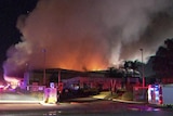 Smoke billows from a large factory with a fire truck in the foreground