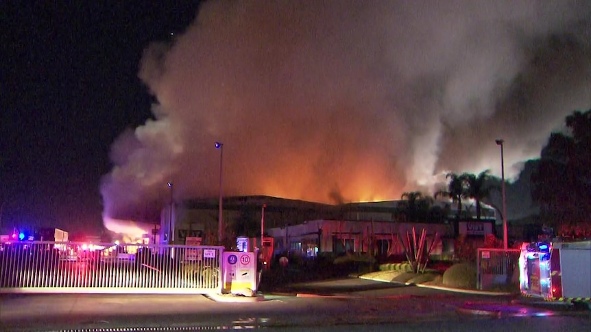 Smoke billows from a large factory with a fire truck in the foreground