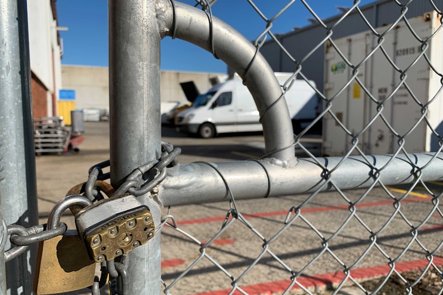 Two padlocks around chain-link keep a wire gate shut.