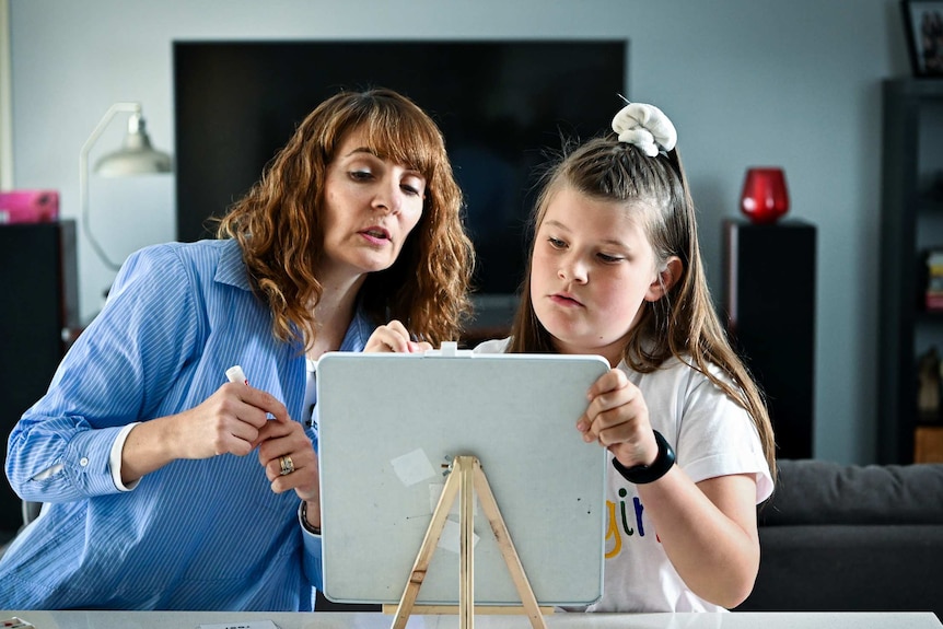 Jorja Mackie (9) writes on a white board as her reading tutor Paula Sciré offers guidance during a lesson at her home.