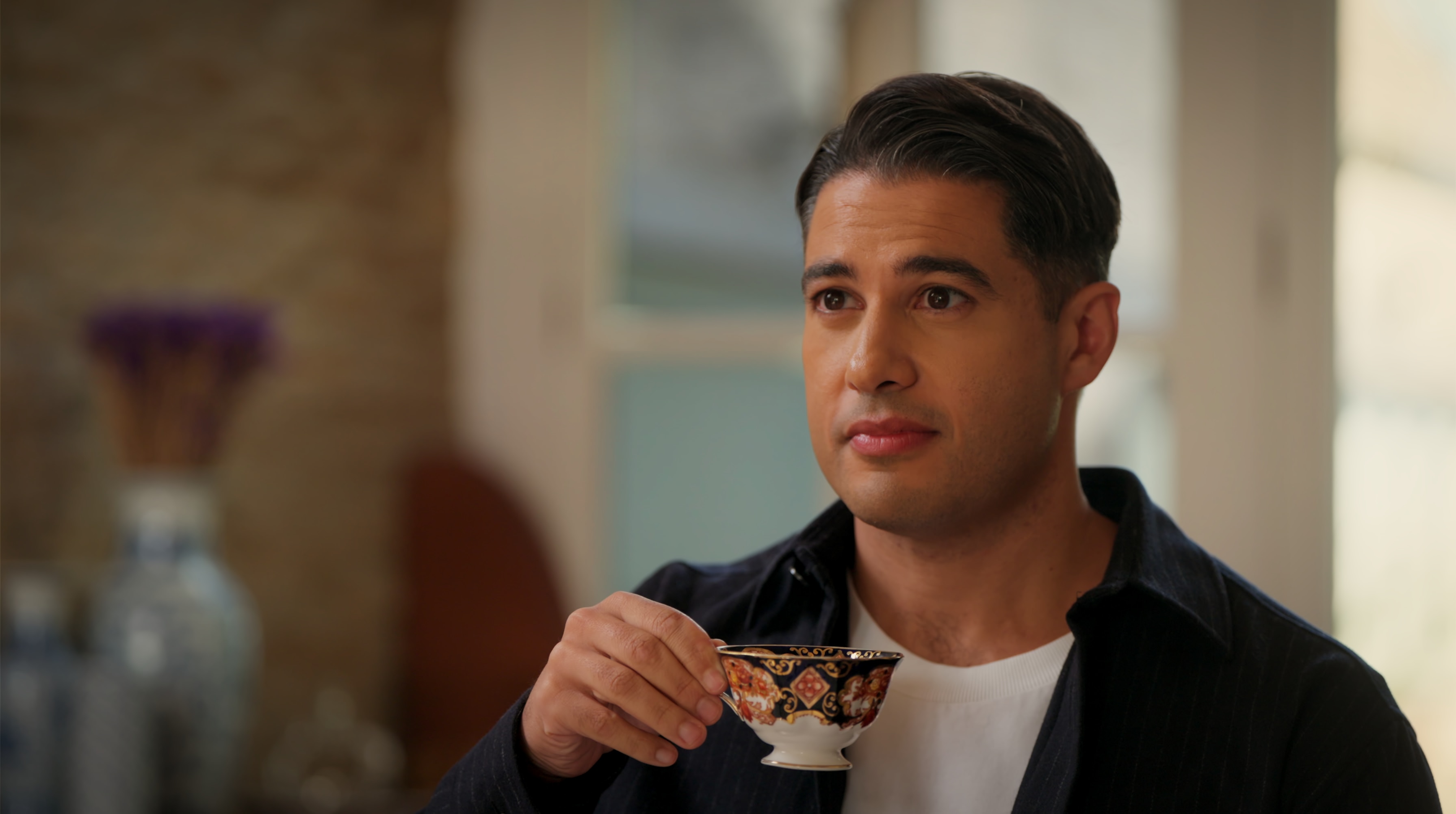 Marc Fennell holds a delicate teacup as he listens intently to someone off screen.
