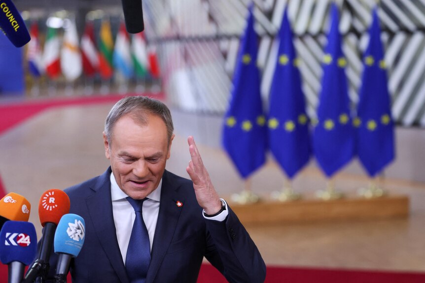 Donald Tusk with his arm raised standing in front of EU flags. 