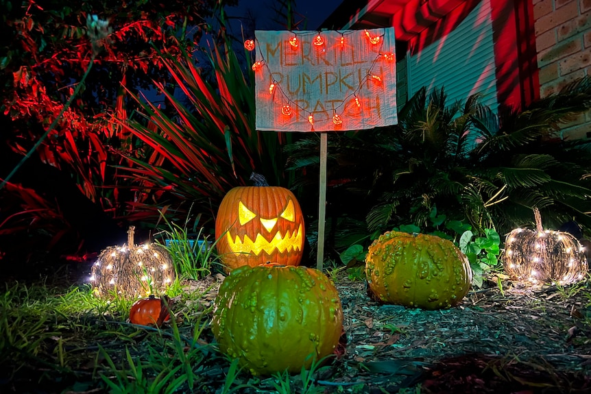 five pumpkins outside a home at night with an ominously lit sign