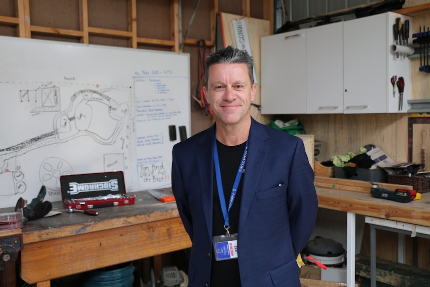 Cam Wiseman wearing a navy blue suit jacket and smiling inside a workshop.