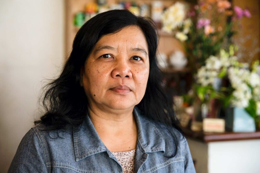 A woman with black hair and wearing a denim jacket with a shirt smiles.