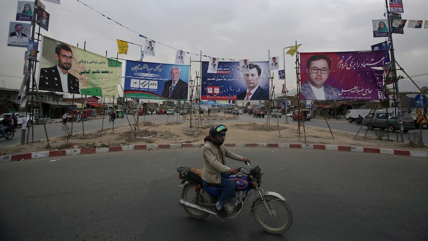A person riding a motorbike through a roundabout passes by four billboards for candidates in the Afghanistan elections.