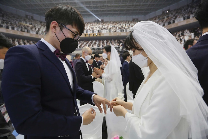 A couple wearing face masks exchanges their rings in a mass wedding ceremony.