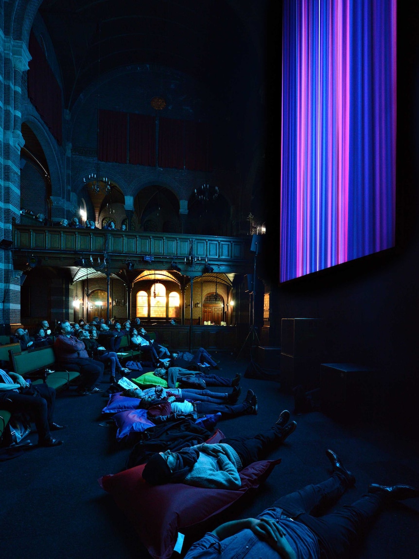 People lay on the floor on cushions looking up at a screen