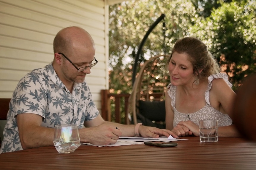 A man and woman look at paperwork while sitting at an outdoor wooden table