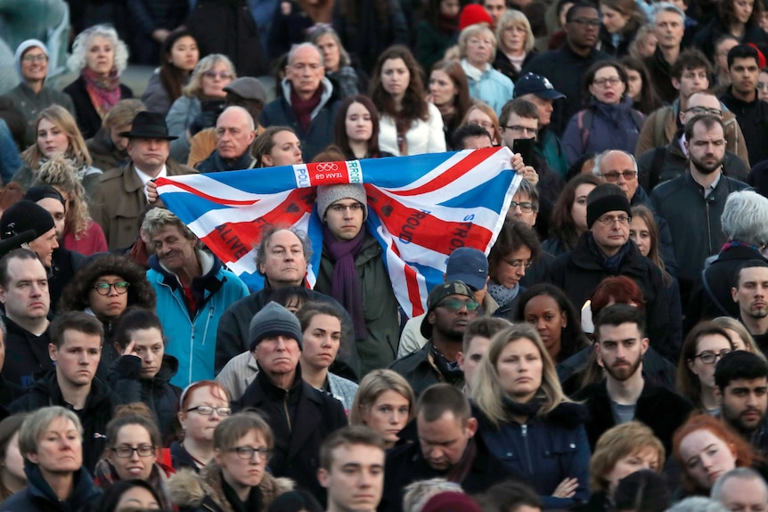 A crowd of people attend a vigil in Trafalgar Square for the London Attacks, a man in the centre holds a Union Jack flag.