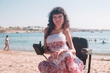Olena wears a pink dress sitting in a wheelchair at the beach