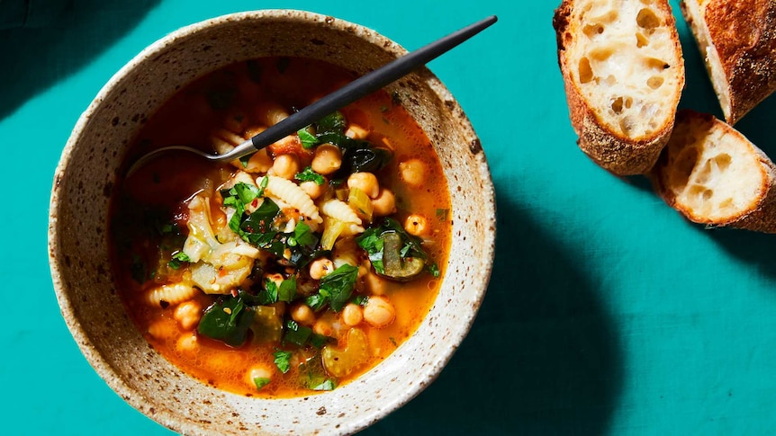 Close-up of a terracotta bowl filled with pasta, chickpea and spinach soup, in a list of winter comfort food recipes.