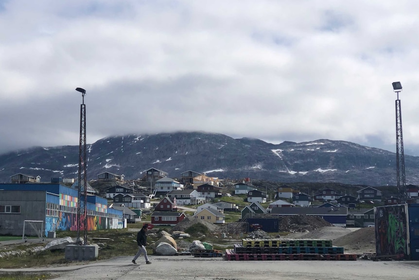 A person walks across a concreted area in the foreground. Behind them is Greenland's capital Nuuk.