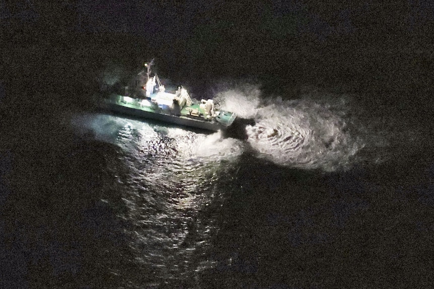 A coast guard ship in the water at night, with a spotlight in the water, looking for wreckage