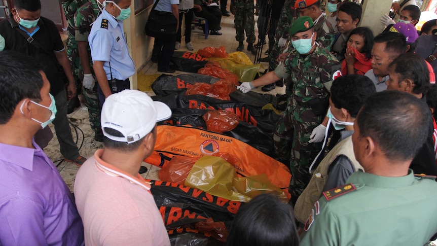Relatives searching for missing family members gather around body bags containing victims retrieved from the crash site of an Indonesian Air Force C-130 Hercules aircraft