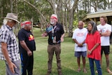 a group of indigenous Australian, five man and one woman standing in a circle in a park discussing something passionately