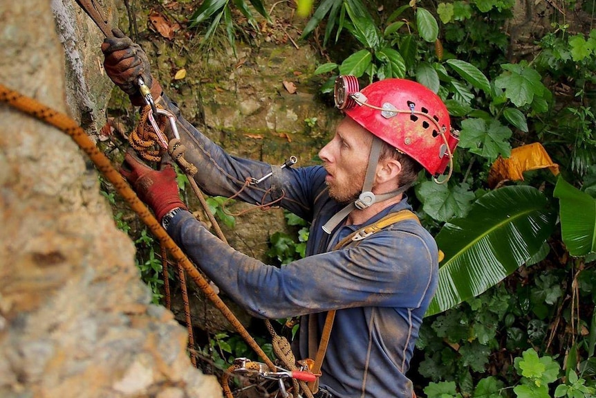 A man in protective gear with harnesses and ropes next to a rock wall