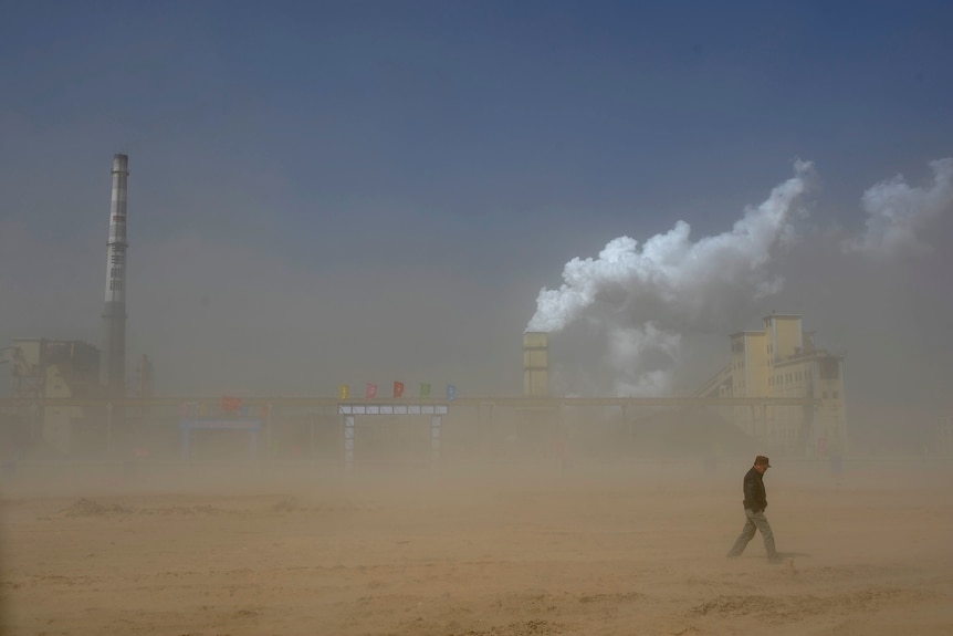 A man is seen walking past a coal power plant in a dusty, barren landscape