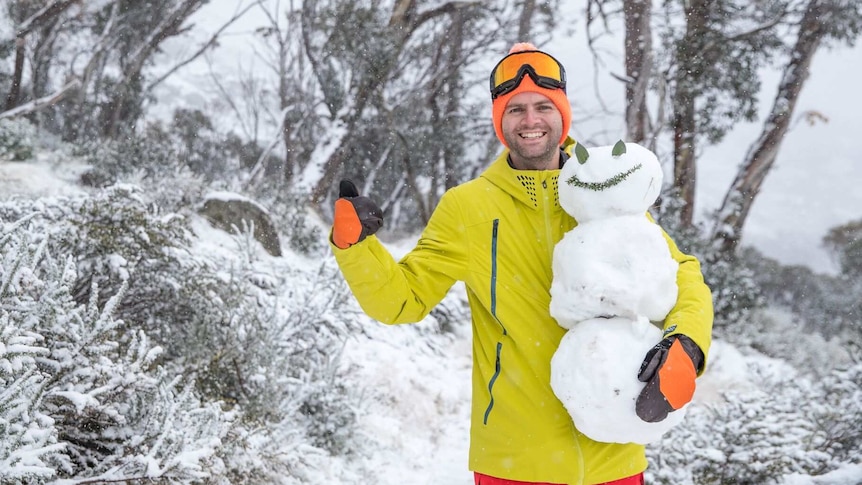 A man in the snow holding a snowman