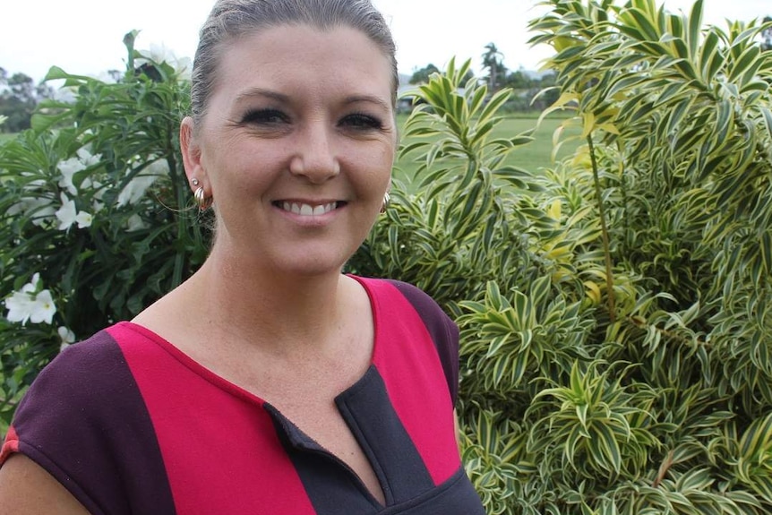 A woman stands in front of tropical plants, with a paddock in the background.