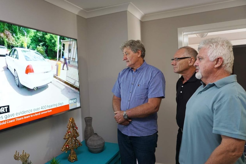 Three men looking at a TV.