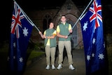 Two Australian athletes stand in front of a church at night, holding Australian flags.