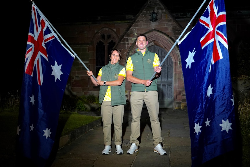 Two Australian athletes stand in front of a church at night, holding Australian flags.