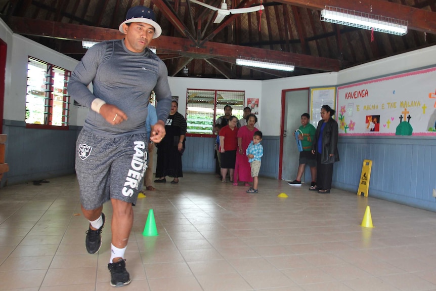Lafaele is running inside a school hall, demonstrating how he wants the next game to be played.