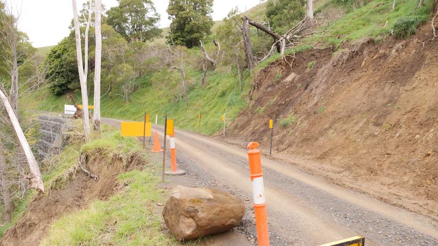A thin dirt road with barriers on the side. Either side of the road is gashes in the landscape where a landslide happened.