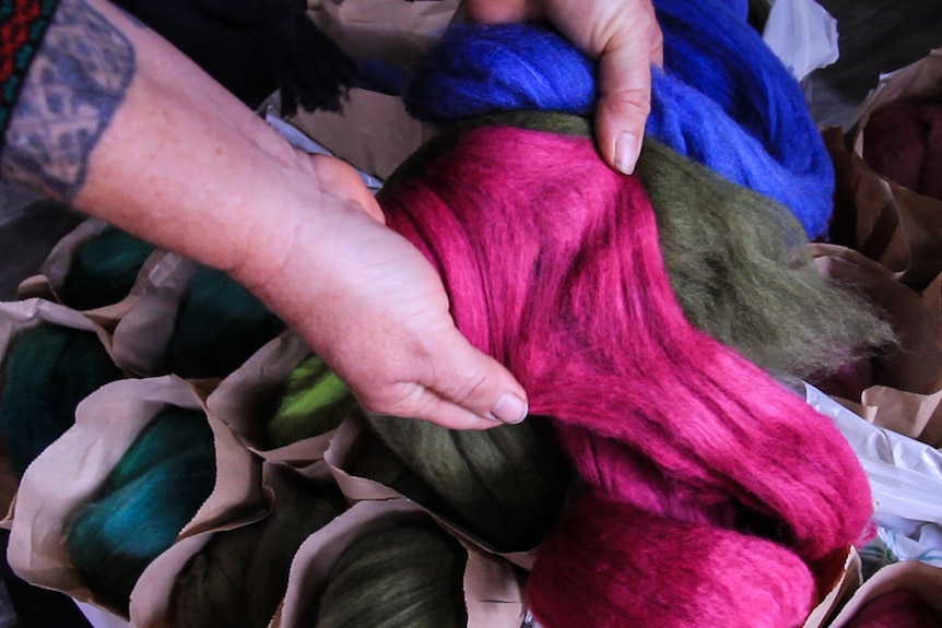 A close-up shot of a woman's hands holding vibrantly died wool.