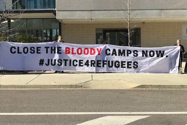 Protesters hold a close the banner that reads "close the bloody camps now" outside the ACT Magistrates Court.