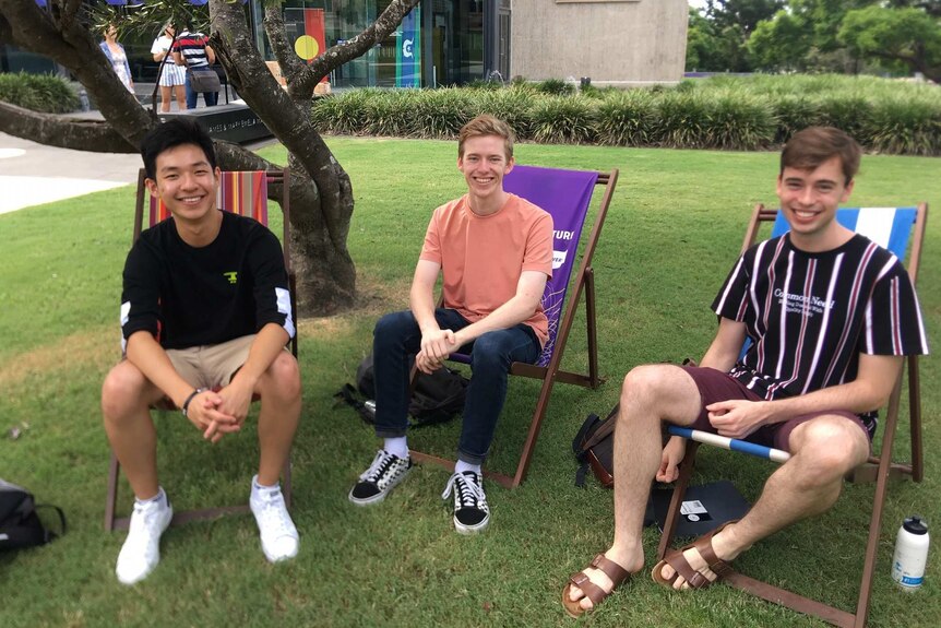 Three young men sitting in chairs on grass and smiling