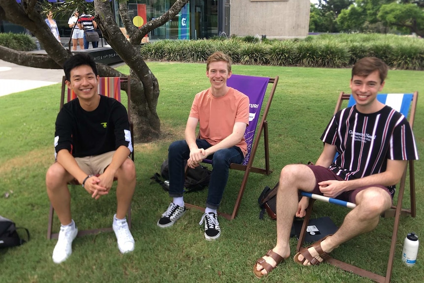 Three young men sitting in chairs on grass and smiling