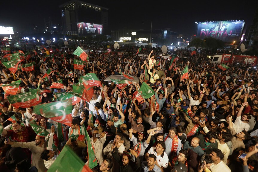 Une grande foule de Pakistanais se rassemblent à l'extérieur le soir, avec de nombreux drapeaux ondulés du parti politique Tehreek-e-Insaaf