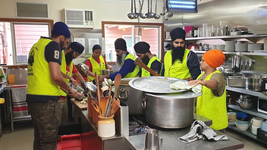 Seven sikhs wearing yellow vests preparing food in a commercial kitchen
