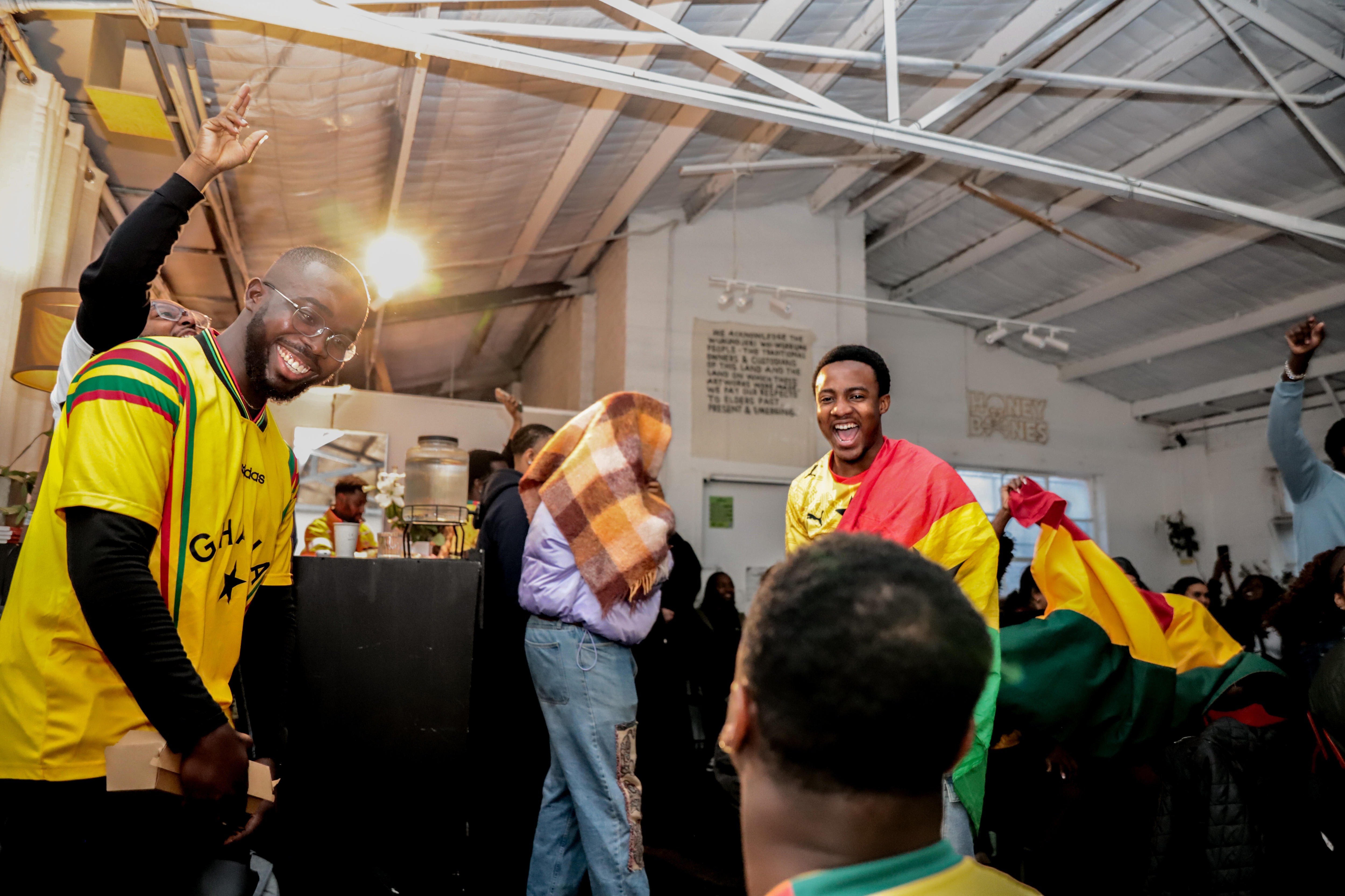 A man wearing a yellow t-shirt with red and green stripes and another draped in a yellow, red and green flag dance and smile.