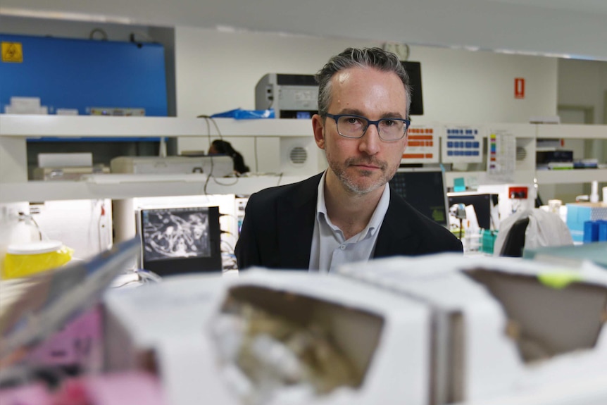 Dr JIm Newcome stands in a lab behind shelves of PPE.