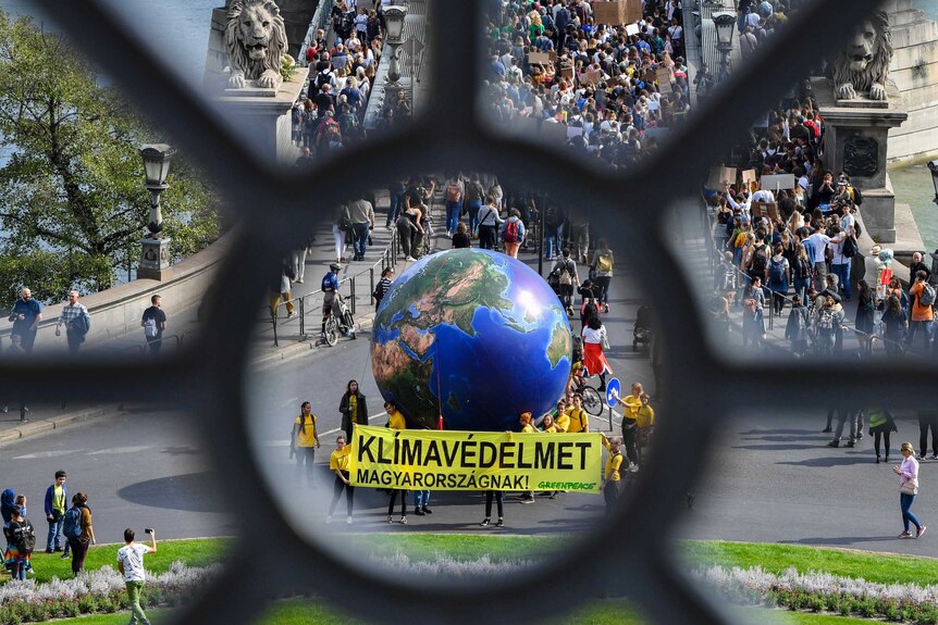 A photo taken through a building show a globe and protesters holding a yellow banner at a bridge with statues of lions.