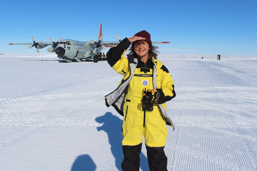 Fiona shields her face from the sun, as she stands in front of a plane on a snowy runway.