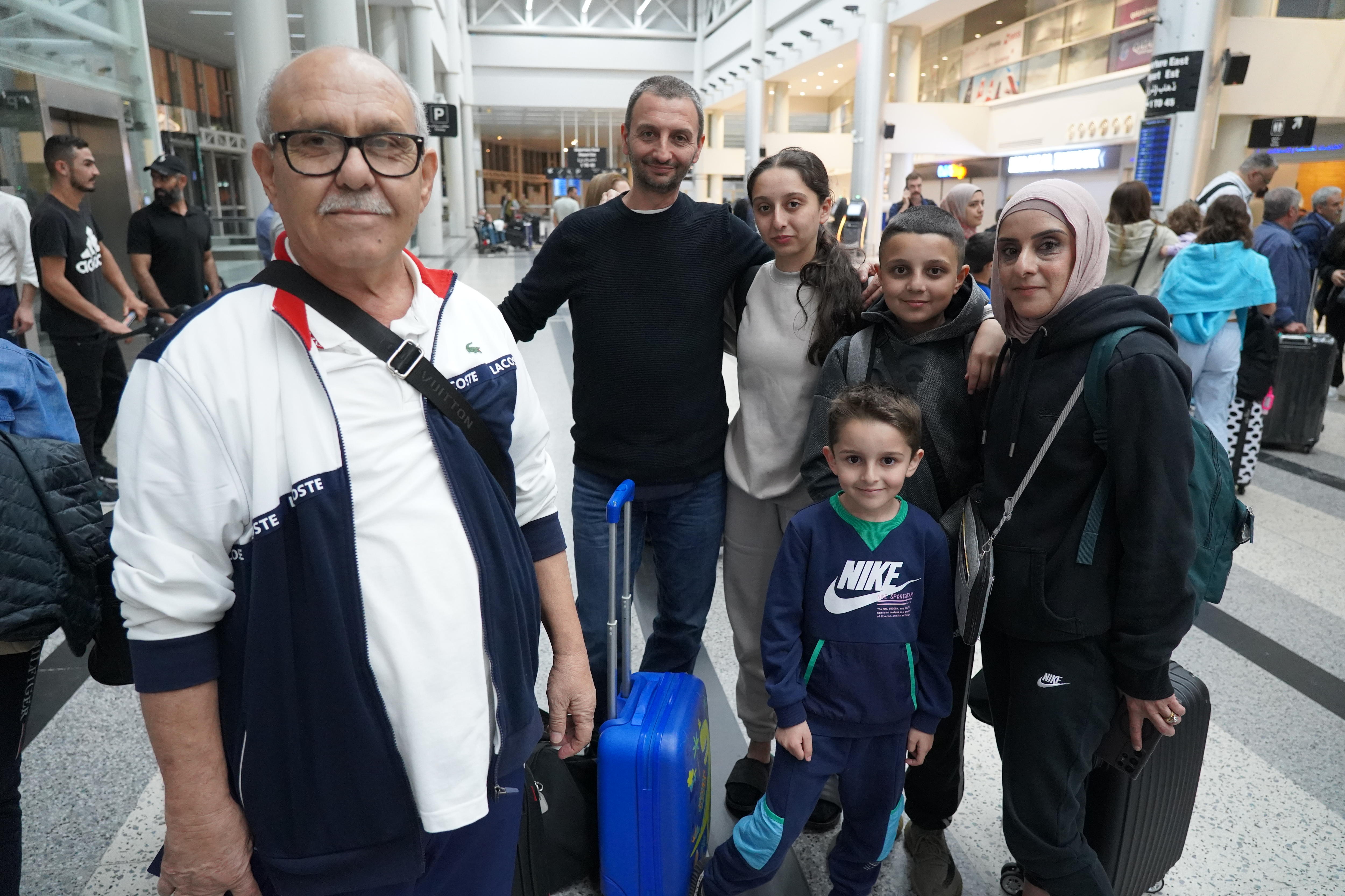 A man in a white shirt with five family members standing behind him at an airport. 