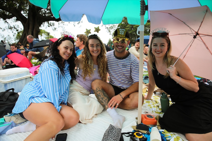 Four people sitting together under umbrellas with sunglasses and new year headbands