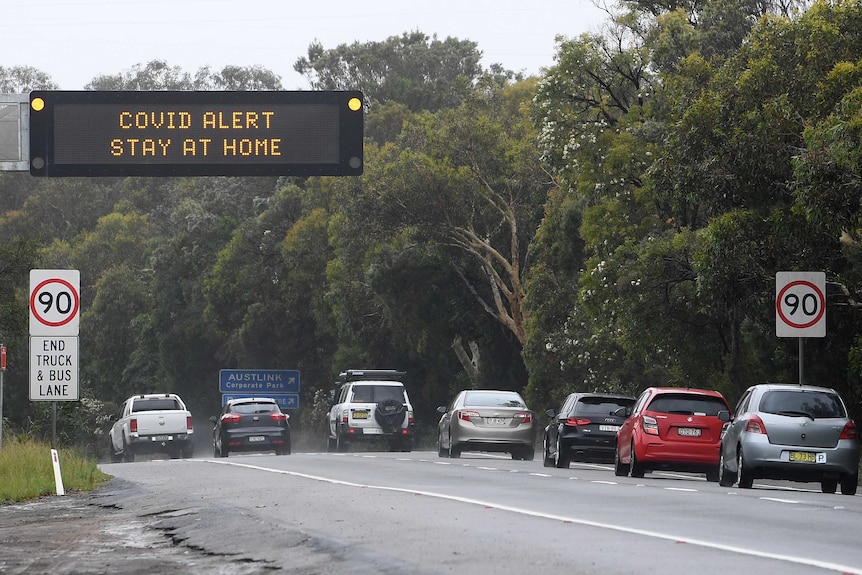 Cars drive under a sign saying "COVID ALERT STAY AT HOME"